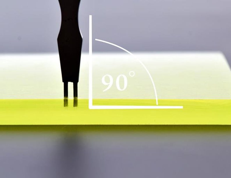 May include: A black tool with two prongs is being used to test the 90 degree angle of a yellow surface.