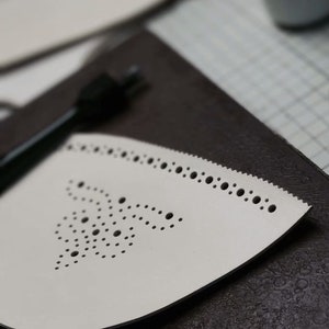 May include: A white ironing board cover with a decorative pattern of small holes. The cover is on a dark brown surface.