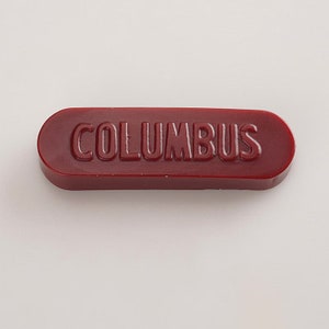 K&ouml;nnte beinhalten: Ein rotes Siegelwachs mit dem Wort "COLUMBUS" in wei&szlig; gepr&auml;gt.