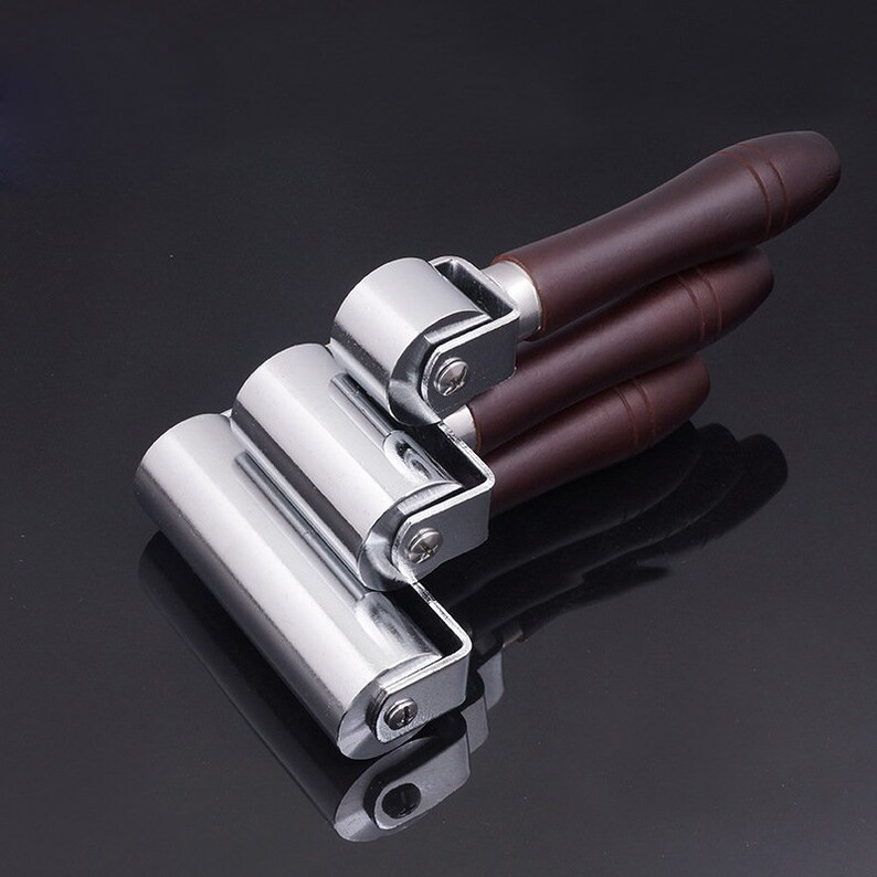 May include: A set of three chrome roller tools with brown wooden handles. The rollers are different sizes and are attached to a metal frame.