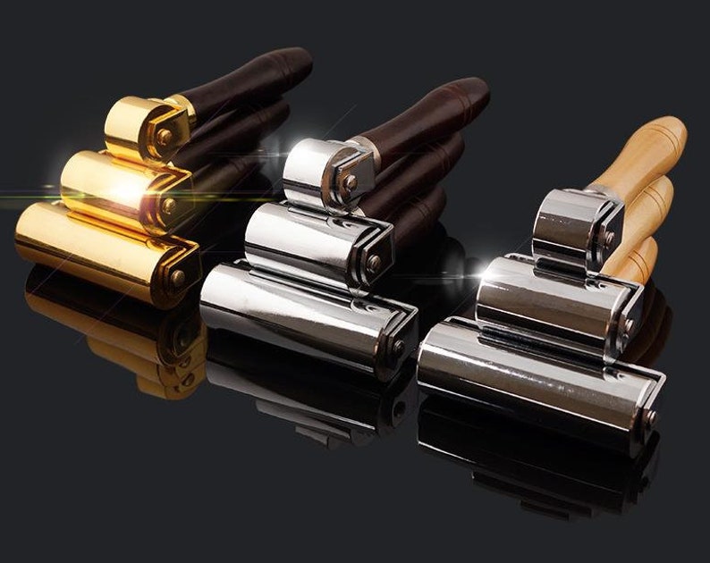 May include: Three rolling tools with wooden handles. The tools have different finishes: gold, silver, and chrome. The tools are stacked on top of each other.