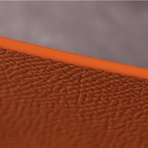 May include: Close-up of a textured orange leather surface. The leather has a fine grain pattern.