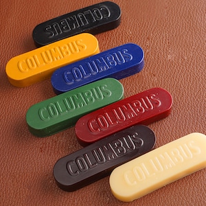 K&ouml;nnte beinhalten: Sechs Siegelwachsst&auml;be in verschiedenen Farben: Schwarz, Gelb, Blau, Gr&uuml;n, Rot und Creme. Jeder Stab hat das Wort "COLUMBUS" gepr&auml;gt.