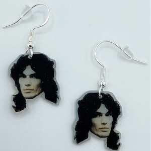 May include: A pair of silver dangle earrings with a black and white photo of a man's face on each earring.