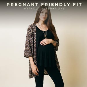 May include: A black tank top and black leggings paired with an open-front kimono featuring a dark patterned print. The text PREGNANT FRIENDLY FIT WITHOUT ALTERATIONS is displayed at the top. A layered silver necklace with a crescent moon pendant is worn.