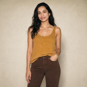 Puede incluir: Una camiseta sin mangas de color amarillo mostaza con textura acanalada y cuello redondo, combinada con pantalones vaqueros de color marr&oacute;n oscuro con cierre de botones y bolsillos delanteros. La parte superior tiene un corte holgado.