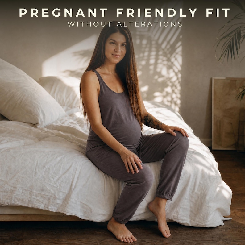 Puede incluir: Un conjunto de camiseta sin mangas gris oscuro y pantalones de ch&aacute;ndal a juego. El texto PREGNANT FRIENDLY FIT WITHOUT ALTERATIONS aparece en la parte superior. La prenda presenta un cuello redondo y pu&ntilde;os en los tobillos.