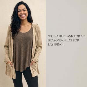 Puede incluir: Un c&aacute;rdigan beige con capucha, mangas largas y dos bolsillos delanteros, usado sobre una camiseta sin mangas marr&oacute;n y leggings negros. El texto a la derecha dice: VERSATILE TANK FOR ALL SEASONS GREAT FOR LAYERING!