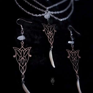 Peut inclure: Un ensemble de collier et boucles d'oreilles argentés sur fond noir. Le collier présente plusieurs chaînes délicates et de petites perles transparentes. Les boucles d'oreilles et le pendentif ont un motif floral stylisé avec un long charme blanc.