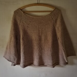 Peut inclure: Un pull en tricot beige à la coupe ample et aux manches bouffantes. Le pull a un col rond et un motif de dentelle délicat.