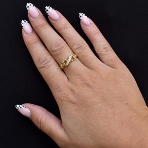 May include: A gold ring with three small diamonds and a decorative filigree design. The ring is on a hand with manicured nails, painted with a white and black polka dot design.