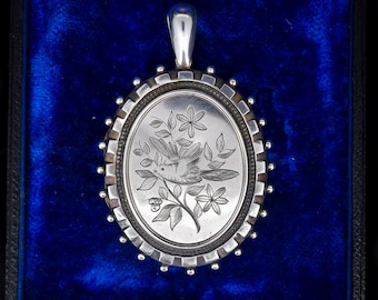 Pode incluir: Medalha de prata com um design gravado de um pássaro empoleirado em um galho com flores e bagas. A medalha tem uma borda de contas.