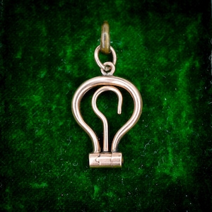 Peut inclure: Pendentif doré en forme d'ampoule, avec un motif en boucle à l'intérieur. Il comporte une petite boucle en haut pour une chaîne et une base cylindrique. Le fond est vert foncé.