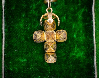 May include: A gold-colored cross pendant with intricate geometric designs. The cross is made of several square-shaped segments, each with detailed patterns. The pendant hangs from a small loop and is set against a dark green velvet background.
