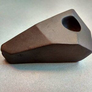 Op de afbeelding: Een zwarte keramische pijp met een geometrische vorm en een rond gat aan de bovenkant.