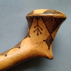 Puede incluir: Objeto de color claro, posiblemente de madera, con intrincados patrones geométricos negros. El diseño incluye líneas, triángulos y rombos, creando una apariencia detallada y artística. El objeto tiene una forma curva.