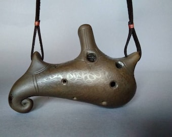 May include: A brown ceramic ocarina with a decorative design and multiple finger holes. It has a leather cord with copper accents for hanging.