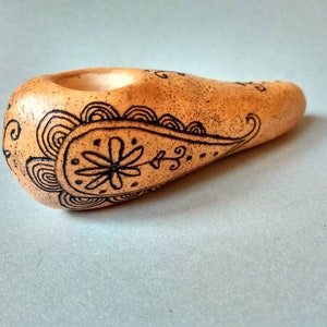 May include: A hand-painted ceramic pipe with a brown glaze and a black paisley design. The pipe has a small bowl and a long, curved stem.