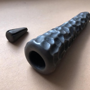 May include: A black ceramic pipe with a textured surface and a round opening. The pipe is about 6 inches long and has a small, black ceramic cap.