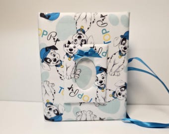 May include: A white photo album with a blue ribbon. The cover features a repeating pattern of Dalmatian puppies wearing blue hats and the text "Top Pup".