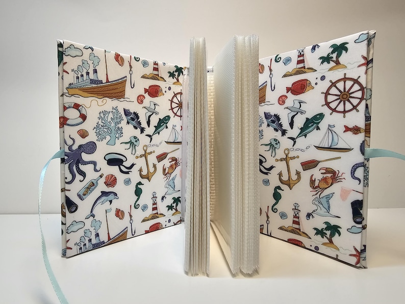 Puede incluir: Un &aacute;lbum de fotos blanco con tem&aacute;tica n&aacute;utica. La portada presenta una variedad de ilustraciones, incluyendo un barco, anclas, peces y conchas marinas. El &aacute;lbum es perfecto para guardar recuerdos de unas vacaciones en la playa.