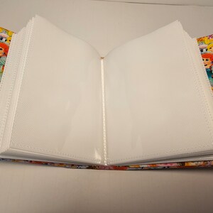 Puede incluir: Un &aacute;lbum de fotos blanco con fundas de pl&aacute;stico transparente para guardar fotos. La cubierta est&aacute; hecha de tela y presenta una impresi&oacute;n colorida de princesas Disney.