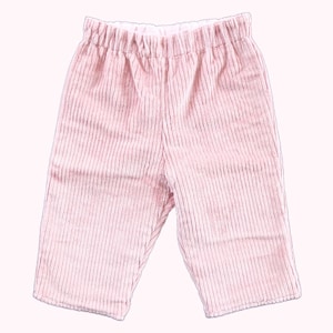 May include: Pink corduroy pants with an elastic waistband. The pants have vertical stripes and a relaxed fit, suitable for casual wear. The soft, pastel color and comfortable design make them ideal for everyday use.