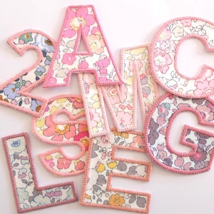 Peut inclure: Un ensemble de lettres et de chiffres en tissu rose et blanc avec un motif floral. Les lettres sont A, C, E, G et L. Les chiffres sont 2 et 3.