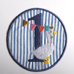 May include: Embroidered patch featuring a blue number 1 with a goose wearing a party hat. The goose is decorated with a banner of colorful flags. The patch has a blue and white striped background and a dark blue border.