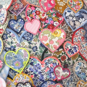 Può includere: Una collezione di cuori in tessuto con vari motivi floreali e colori, tra cui rosa, blu e giallo. I cuori sono cuciti insieme per creare un design a patchwork.