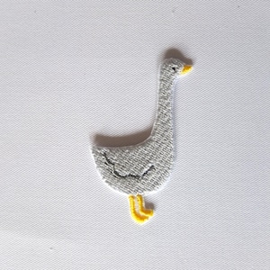 Op de afbeelding: Een grijze geborduurde gans met gele poten en snavel. De gans staat op een witte achtergrond.