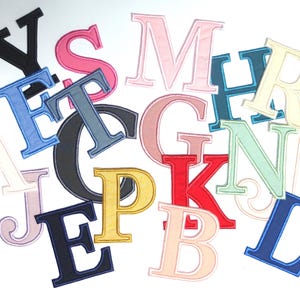 Peut inclure: Diverses lettres brodées en tissu, de couleurs variées : bleu, rose, jaune et noir. Les lettres sont de différentes polices et tailles, disposées sur un fond blanc. Idéales pour les loisirs créatifs ou la personnalisation.