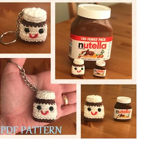 Può includere: Schema di amigurumi all'uncinetto per un portachiavi a forma di barattolo di Nutella. Lo schema include le istruzioni per realizzare un piccolo barattolo di Nutella con un coperchio bianco e un corpo marrone. Il barattolo ha un viso di cartone animato carino con occhi neri e un sorriso rosso. Lo schema include anche le istruzioni per realizzare un piccolo portachiavi.