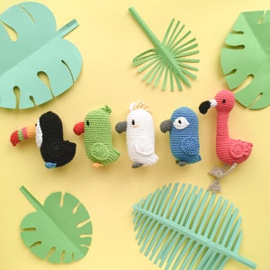 May include: A set of six crocheted stuffed animals, including a toucan, parrot, cockatoo, blue jay, and flamingo. The animals are arranged in a row on a yellow background with green paper leaves.