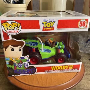 Op de afbeelding: Een Funko Pop! Rides figuur met Woody uit Toy Story in een groene en blauwe RC auto. De doos toont de Toy Story en Pop! Rides logo's. Het figuur is nummer 56.
