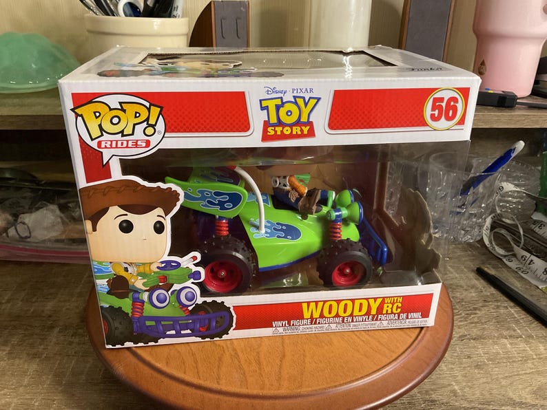 Op de afbeelding: Een Funko Pop! Rides figuur met Woody uit Toy Story in een groene en blauwe RC auto. De doos toont de Toy Story en Pop! Rides logo's. Het figuur is nummer 56.