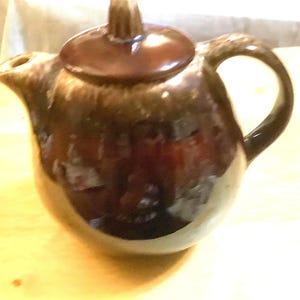 May include: A brown ceramic teapot with a lid and a handle. The teapot has a mottled glaze with brown and white speckles.