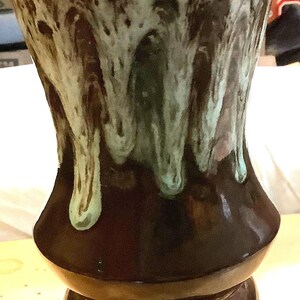 May include: A brown ceramic vase with a green and white marbled glaze. The vase has a wide base and a narrow neck.