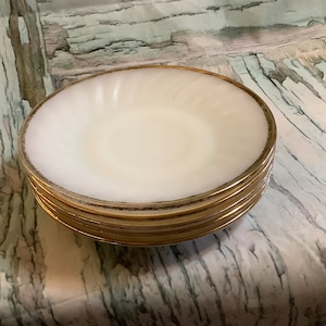 May include: A stack of five white bowls with a gold rim. The bowls are made of glass and have a slightly rippled surface.