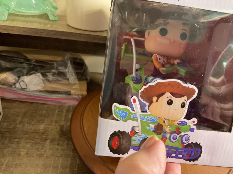 Op de afbeelding: Een Funko Pop! figuur van Woody uit Toy Story in een doorzichtige displaydoos. Woody wordt afgebeeld in een go-kart met een groen en blauw ontwerp. Het figuur zit in een doorzichtige plastic display.