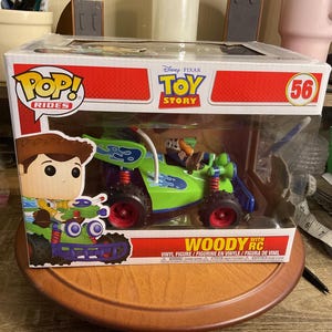 Op de afbeelding: Een Funko Pop! Rides figuur met Woody uit Toy Story in een groene en blauwe RC auto. De doos heeft het Disney Pixar Toy Story logo en het nummer 56. Het figuur is een vinyl figuur.
