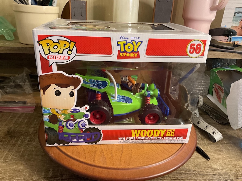 Op de afbeelding: Een Funko Pop! Rides figuur met Woody uit Toy Story in een groene en blauwe RC auto. De doos heeft het Disney Pixar Toy Story logo en het nummer 56. Het figuur is een vinyl figuur.