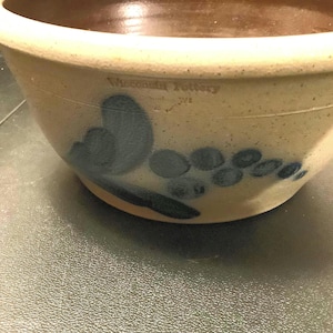 May include: A large, cream-colored stoneware bowl with a blue and black floral design. The bowl is marked "Wisconsin Pottery" on the side.