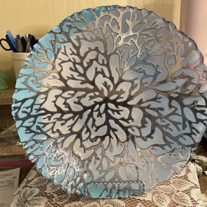 以下が含まれることがあります： サンゴ礁のデザインが施された装飾ガラスプレート。プレートは、ライトブルーとシルバーの色使いです。サンゴのデザインは隆起しており、テクスチャード加工された表面を作り出しています。プレートは丸く、波状の縁があります。