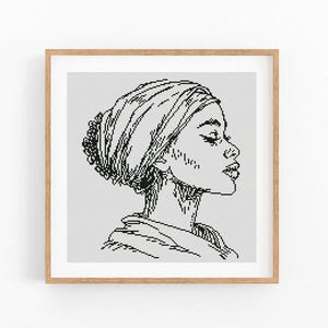 May include: A framed black and white cross-stitch portrait of a person in profile, wearing a head wrap. The artwork is set against a white background, framed in a light brown wooden frame.