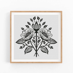 Könnte beinhalten: Schwarz-weißes Blumen-Kreuzstichmuster in einem hellbraunen Holzrahmen. Das Design zeigt drei stilisierte Blumen mit detaillierten Blütenblättern und Blättern, die symmetrisch angeordnet sind. Das Kunstwerk ist vor einem weißen Hintergrund.