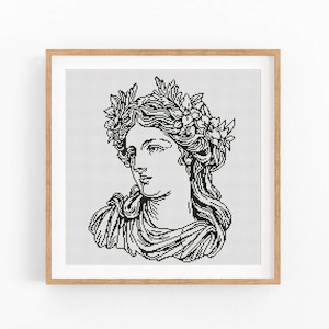 May include: Black and white cross-stitch art of a classical female bust wearing a laurel wreath. The artwork is framed in a light brown wooden frame. The bust is rendered in a detailed, grayscale style, with flowing hair and a serene expression.