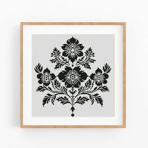 May include: A framed cross-stitch pattern featuring a symmetrical floral design in black against a white background. The artwork is enclosed in a light brown wooden frame, showcasing a detailed botanical motif.