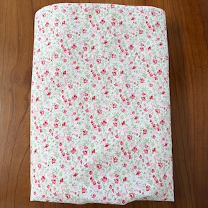 Peut inclure: Un morceau de tissu rectangulaire blanc orné d'un motif dense et répétitif de petites fleurs roses et rouges avec des tiges et des feuilles vertes délicates. Le textile est plié en une forme compacte et nette, révélant l'imprimé floral.