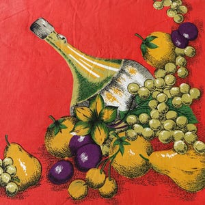 May include: A red fabric featuring a printed illustration of a glass bottle surrounded by various fruits including yellow pears, green grapes, purple plums, and yellow citrus fruits with green leaves, arranged in a dense, colourful composition.